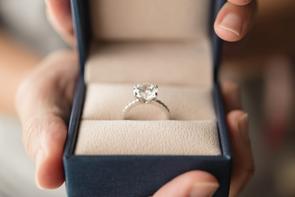 Hands holding diamond engagement ring in jewelry box.