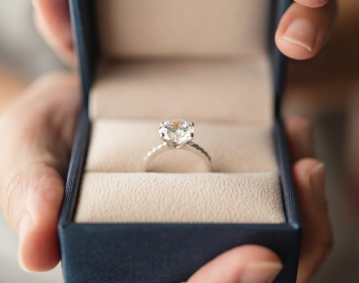 Hands holding diamond engagement ring in jewelry box.